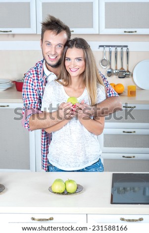 Cooking with love. Beautiful pair is standing on the kitchen  and hugging. Bothe are looking directly to the camera and smile