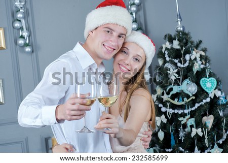 Merry Christmas. Young and beautiful pair is standing in festive New Year living room with glasses of champagne, both are hugging and smiling. Ideal feeling before Christmas and New Year