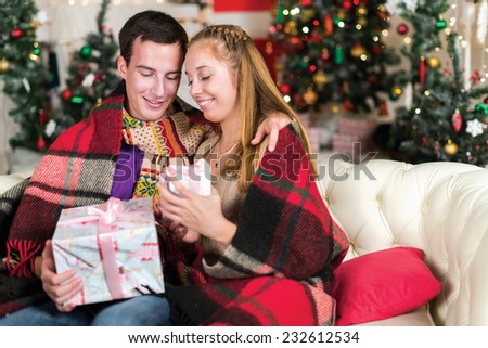 Fun before Christmas. Young and beautiful pair is having fun with New Year presents in the living room. Girl is holding box with New Year presents