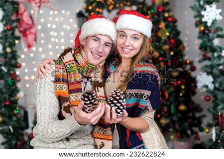 Love on Christmas. Loving couple is standing in the festive New Year living room and smiling. Both are holding cones