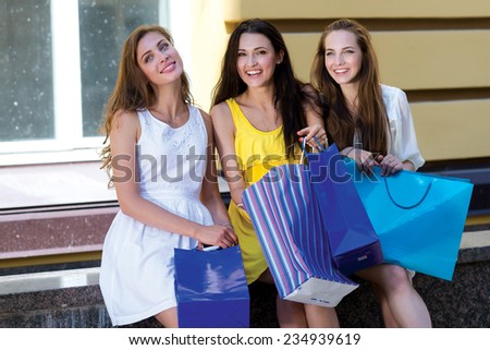 Happy about the shopping and sales. Three young and attractive women are sitting with shopping bags. Pretty girls are having rest after successful shopping day in a mall