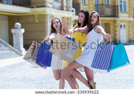 Lets go shopping. Three young and attractive women are standing on the street with shopping bags. Girls are smiling and looking forward happily, because of their purchases in a shopping mall