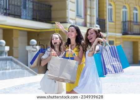Shopping and sales is a great fun. Three young and attractive women are standing on the street with shopping bags. Girls are smiling and looking forward happily