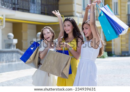 Happy emotions about shopping sales propositions. Three young and attractive women are standing on the street with shopping bags. Girls are smiling and looking forward happily