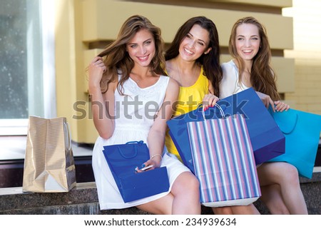 Great shopping day with friends, shops and sales. Three young and attractive women are sitting with shopping bags. Pretty girls are having rest after successful shopping day in a mall