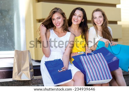 Happy about the shopping and sales. Three young and attractive women are sitting with shopping bags. Pretty girls are having rest after successful shopping day in a mall