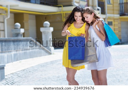 What an awesome shopping sales offer. Two attractive young women are standing on the street with shopping bags and looking on their purchases. Girls are happy and smiling