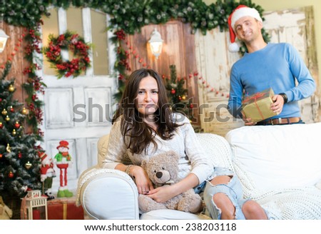 Ready to accept Christmas presents. Couple in love is in festive Christmas decorated living room. Man is ready to give New Year present to his girlfriend. Both are in good Christmas mood