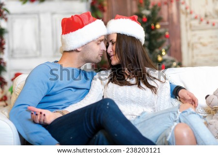 Merry Christmas and Happy New Year. Couple in love is sitting in festive Christmas decorated living room. Both are kissing each other just before New Year