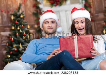 Great Christmas surprise. Couple in love is sitting in festive Christmas decorated living room. Girl is really excited about getting her New Year present