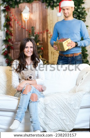 Ready to accept Christmas presents. Couple in love is in festive Christmas decorated living room. Man is ready to give New Year present to his girlfriend.