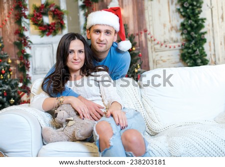 Merry Christmas and Happy New Year. Couple in love is sitting in festive Christmas decorated living room. Both are looking in the camera with smiles and fun New Year mood