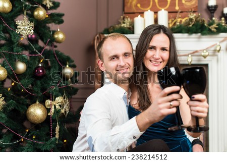 Merry Christmas and Happy New Year. Young beautiful couple in love is celebrating with glasses of champagne in festive New Year living room just before the Christmas.