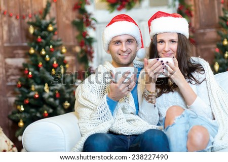 Merry Christmas and Happy New Year. Couple in love is sitting in festive Christmas decorated living room. Both are drinking New Year cacao from pretty Christmas cups