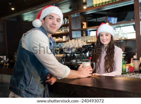 New Year in a bar with beer. Girl bartender is standing in a bar or pub with young handsome man. Both are wearing New Year Santa Claus hats. Great Christmas with beer.