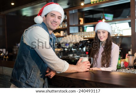 New Year in a bar with beer. Girl bartender is standing in a bar or pub with young handsome man. Both are wearing New Year Santa Claus hats. Great Christmas with beer.