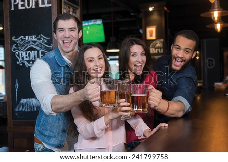 Friends are having fun with beer. Four best friends are standing in a pub and drinking beer with smiles