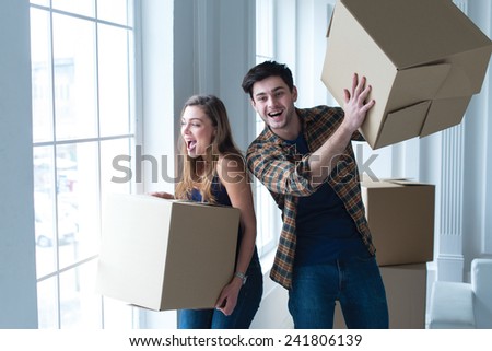 Moving new flat with fun and excitement. Young and beautiful couple is moving to new apartment surrounded with plenty of cardboard boxes. Both are smiling