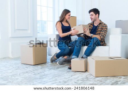 Choosing box for unpacking in new house. Young and beautiful couple is moving to new apartment surrounded with plenty of cardboard boxes