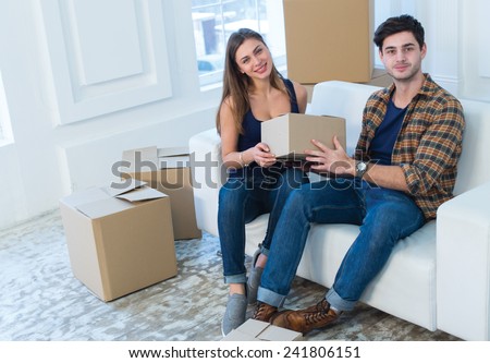 Choosing box for unpacking in new house. Young and beautiful couple is moving to new apartment surrounded with plenty of cardboard boxes