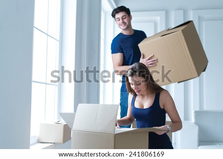 Moving new house. Young and beautiful girl is looking in cardboard box, while moving new flat with her husband