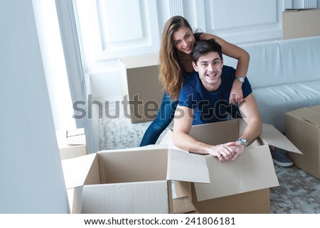 Moving new flat with fun and excitement. Young and beautiful couple is moving to new apartment surrounded with plenty of cardboard boxes. Both are smiling and having fun