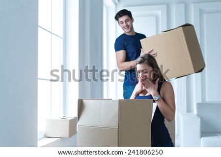 Moving new house. Young and beautiful girl is opening cardboard boxes, while moving new flat with her husband