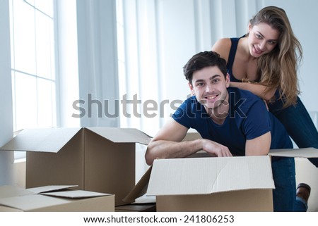 Moving new flat with fun and excitement. Young and beautiful couple is moving to new apartment surrounded with plenty of cardboard boxes. Both are smiling and having fun