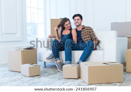Fun while moving new flat. Young and beautiful couple is moving to new apartment surrounded with plenty of cardboard boxes. Both are smiling