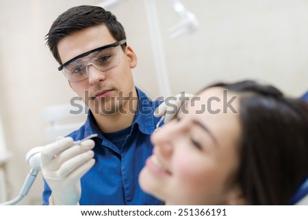 Professional dentist at work. Confident professional doctor dentist is working with patient in dental chair in his medical dental office. Doctor wearing medical clothing.