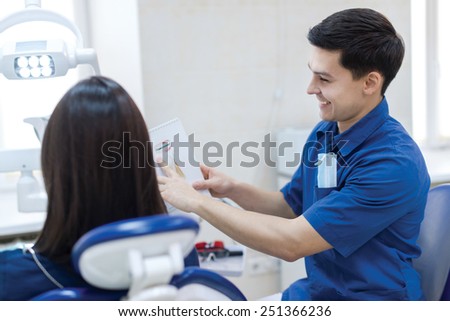 Secret of healthy teeth. Professional doctor shows to the patient picture of healthy teeth in his medical dental office. Doctor wearing medical clothing.