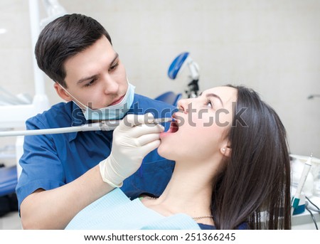 The perfect smile and perfect teeth. Confident professional doctor dentist is sitting and working with his female patient. Doctor wearing medical clothing.