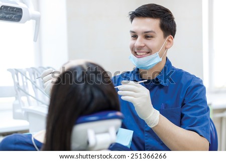 Dentist professional at work. Confident professional doctor dentist is working with patient in dental chair in his medical dental office. Doctor wearing medical clothing.