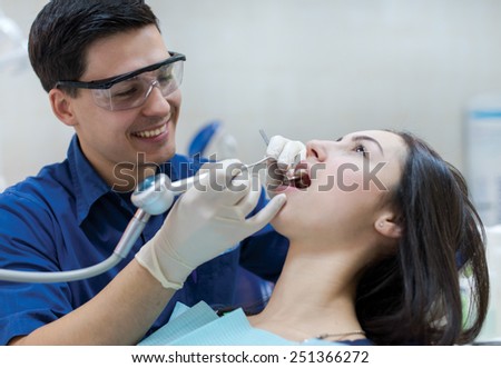 Professional dentist at work. Confident professional doctor dentist is working with patient in dental chair in his medical dental office. Doctor wearing medical clothing.