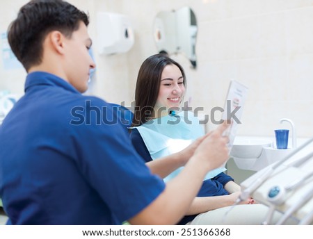 Healthy teeth and smile. Professional doctor shows to the patient picture of healthy teeth in his medical dental office. Doctor wearing medical clothing.