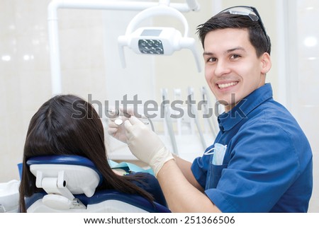 Healthy teeth and smiles. Confident professional doctor dentist is sitting and working with his female patient. Doctor wearing medical clothing.