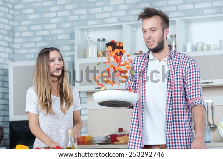 Merry joint cooking. Young and beautiful couple in love preparing meals in the kitchen and look at each other while standing in the kitchen and throw the food in the pan