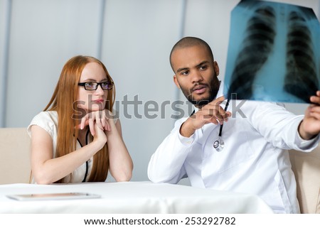 Meeting physician with the patient. Doctor talking with the patient while sitting at a table in the hospital holding an x-ray of the lungs.