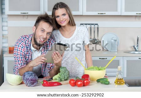 Looking for ideal food recipe. Young and beautiful couple in love is preparing food on the kitchen, while looking for a recipe in tablet