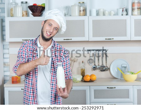 Ideal dairy solution. Portrait of young male cook holding a bottle of milk while standing in the kitchen and smiling at the camera. Milkman. Dairy