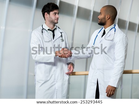Doctors at work. Portrait of two doctors colleagues who are shaking hands, while standing in the hospital in a white coats