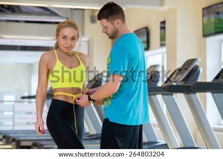 Great training result. Trainer is measuring result of young and beautiful athlete girl in a gym.