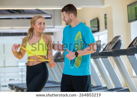 Great training result. Young and pretty woman is measuring her training result, while communicating with her athlete male friend in a gym