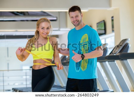 Great training result. Young and pretty woman is measuring her training result. Handsome athlete man is standing next to her and looks forward with smile