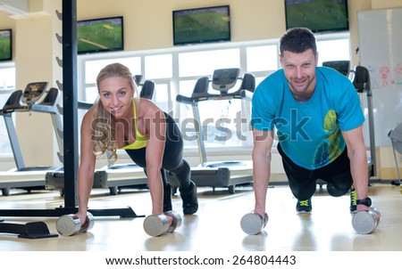 Proper sport shape. Two sportsmen, male and female, are having intensive training in a gym. Both are using dumbbells in a workout. Perfect shape.