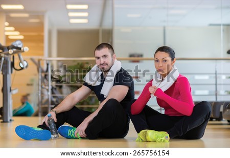 Intensive training together. Couple of young and beautiful people is having workout in a gym. Both are having rest after good workout. Perfect shape. Sportsmen. Hard workout in a gym