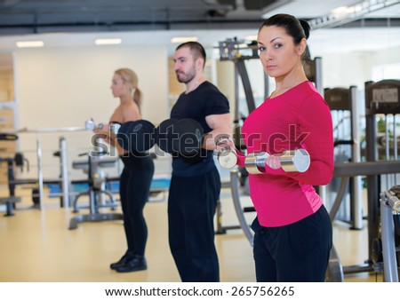 Intensive training together. Portrait of young and pretty athlete girl in a gym. Other people are training on the background. Perfect shape and proper training.