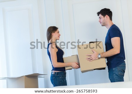 Moving new flat with fun and excitement. Young and beautiful couple is moving to new apartment surrounded with plenty of  boxes. Both are holding packs with their clothes while moving new apartment