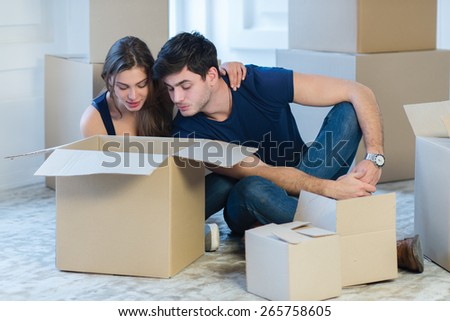 Moving new flat with fun and excitement. Young and beautiful couple is moving to new apartment surrounded with plenty of  boxes. Both are looking inside a box and thinking about future new cozy house
