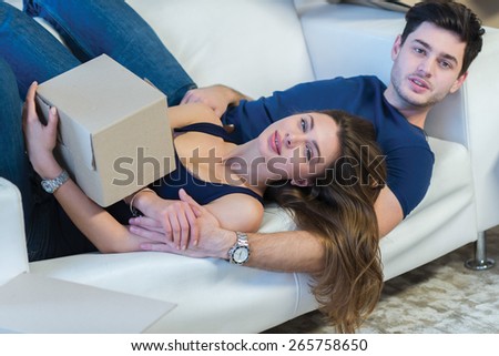 Moving new flat with fun and excitement. Young and beautiful couple is moving to new apartment surrounded with plenty of cardboard boxes. Both are laying on the sofa and dreaming about new cozy house
